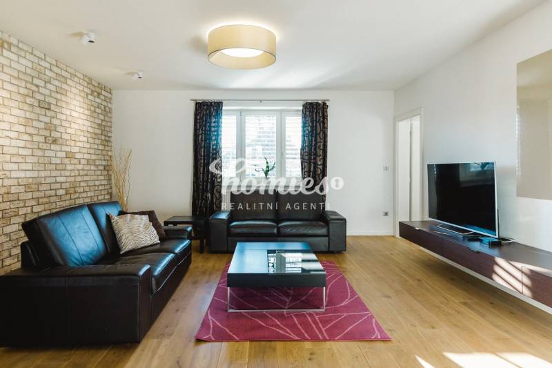 Obývací pokoj s koženou sedačkou, cihlovou stěnou a podlahou s dřevěným dekorem v rodinném domě.