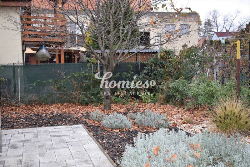 Zahrada u rodinného domu v Nitře, se stromy, trvalkami a dlážděnou plochou.