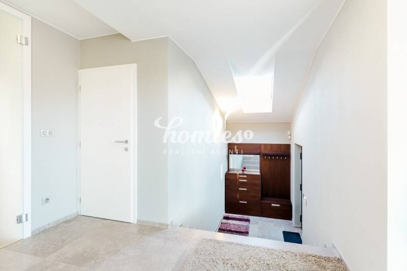 Interiér rodinného domu s dlažbou a bílými stěnami, schodiště a světlík.