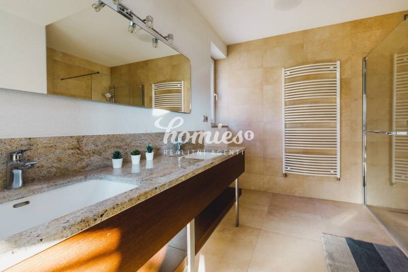 Koupelna v rodinném domě s kamenným umyvadlem, zrcadlem a velkým oknem.