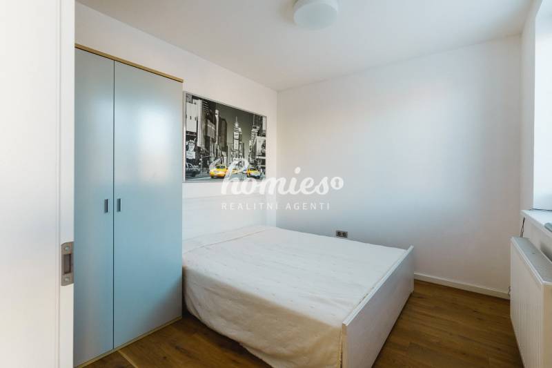 Ložnice v rodinném domě s jednoduchou postelí, skříní a podlahou s dřevěným dekorem.