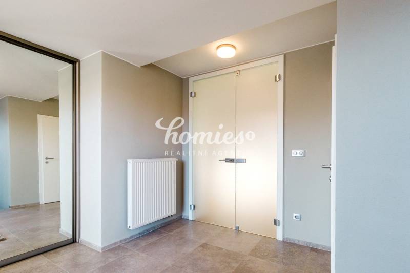 Vstupní hala v rodinném domě s minimalistickým designem, zrcadlem a světlými stěnami.