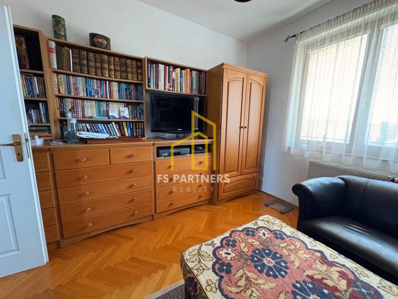 Pokoj ve vícepokojovém bytě s knihovnou, televizí a podlahou s dřevěným dekorem.