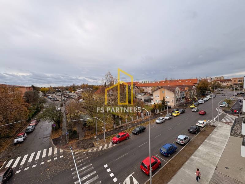 Pohled na ulici s auty a budovami v Komárně, blízko 5 a více pokojového bytu.