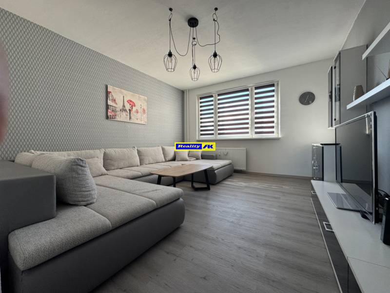 Obývací pokoj v 3-pokojovém bytě s pohovkou a podlahou s dřevěným dekorem.