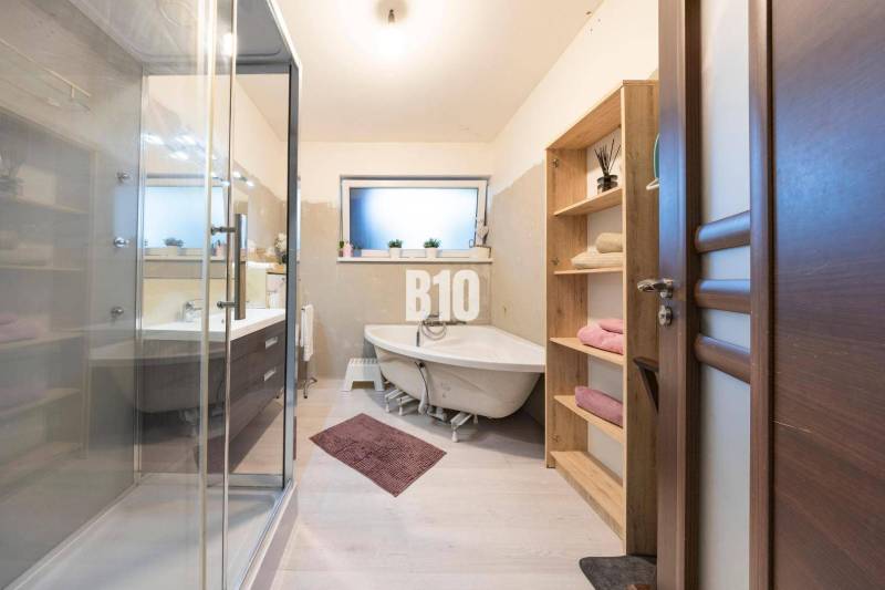 Koupelna v rodinném domě s vanou, sprchovým koutem a nábytkem s dřevěným dekorem.