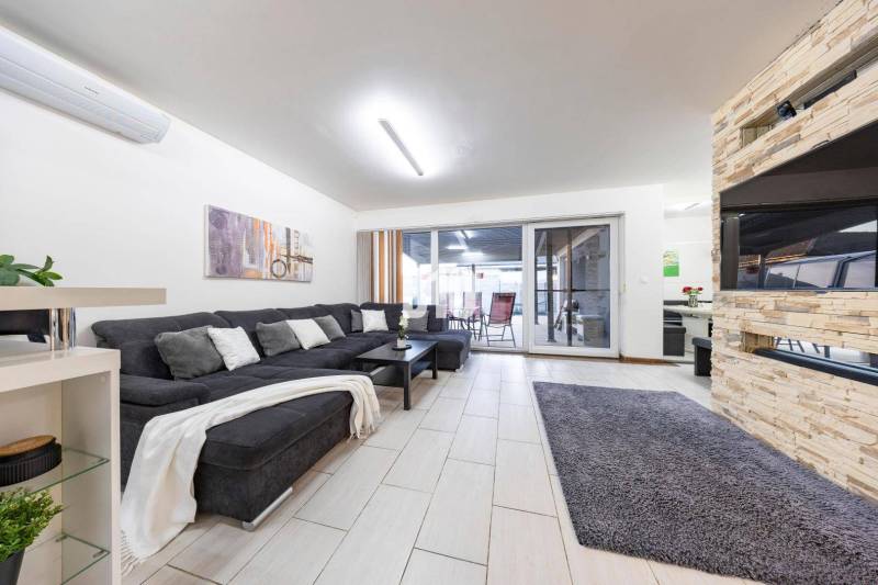 Obývací pokoj rodinného domu s pohovkou, krbem a posuvnými dveřmi na terasu.