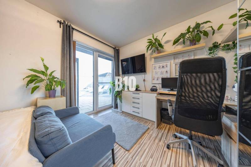 Kancelář v rodinném domě s pohovkou, pracovním stolem, televizorem a rostlinami.