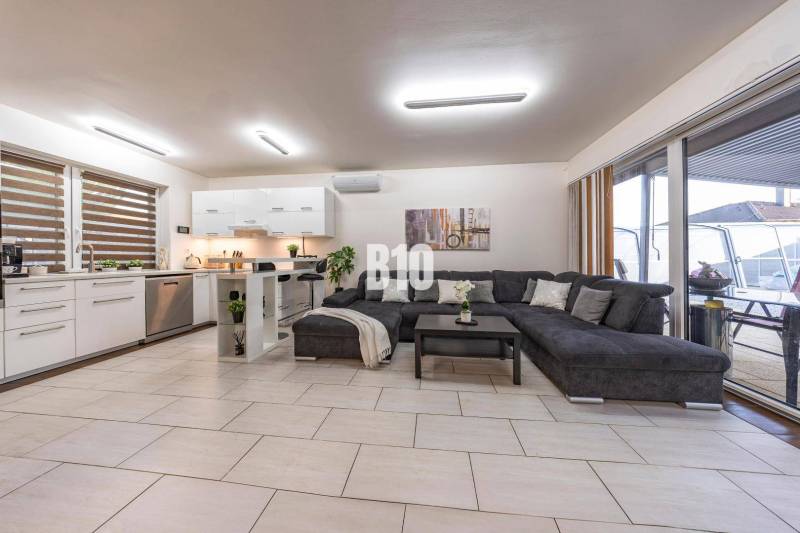 Světlý obývací pokoj v rodinném domě s kuchyní a velkou pohovkou.