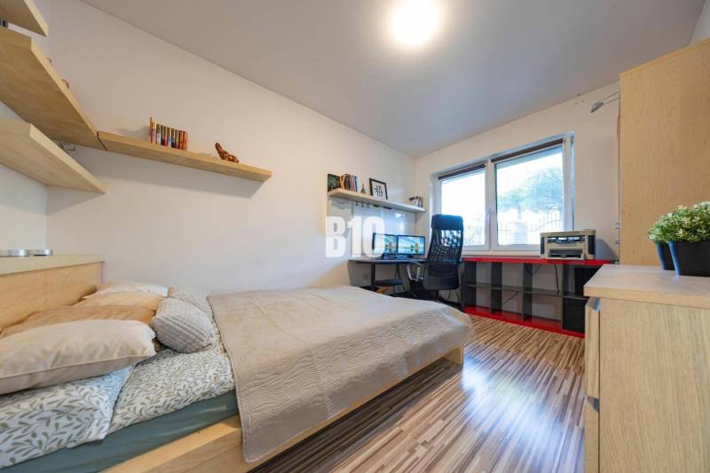 Ložnice v rodinném domě s pracovním stolem, policemi a podlahou s dřevěným dekorem.