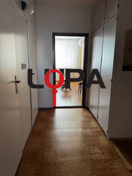 Chodba ve 3-pokojovém bytě s podlahou s dřevěným dekorem vedoucí do světlé místnosti.