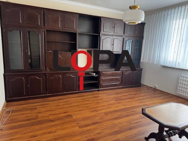 Obývací pokoj v 3-pokojovém bytě s podlahou s dřevěným dekorem, tmavý nábytek.