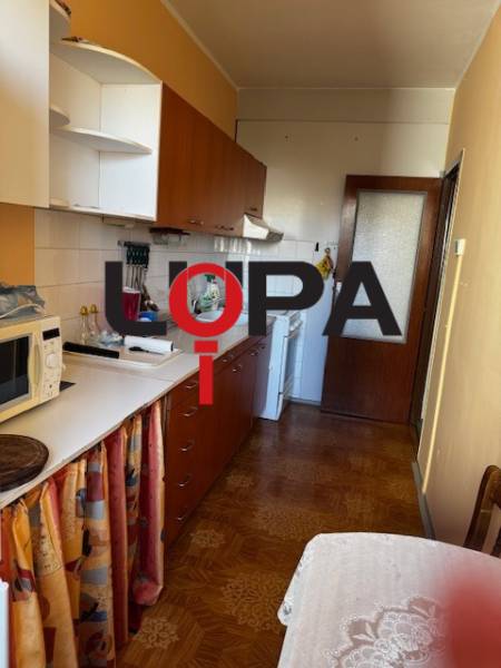 Kuchyně v 3-pokojovém bytě s podlahou s dřevěným dekorem, bílé skříňky, jídelní stůl.