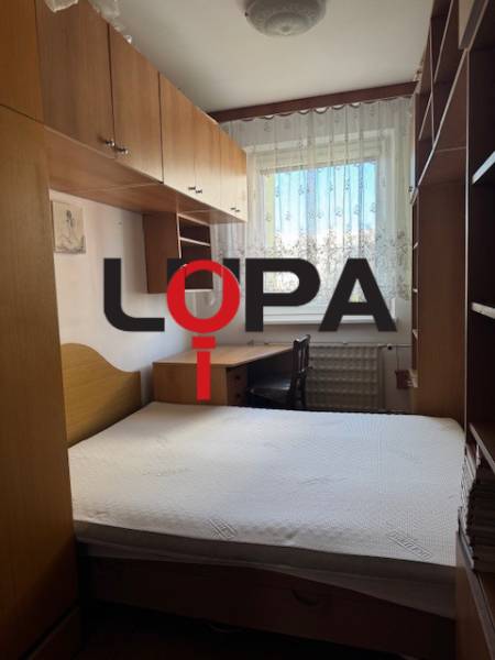 Ložnice v 3-pokojovém bytě s postelí, skříněmi a oknem s krajkovými záclonami.