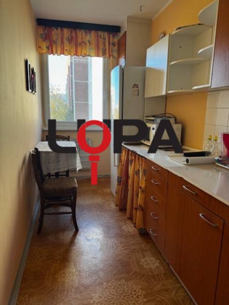 Kuchyně v 3-pokojovém bytě s podlahou s dřevěným dekorem a nábytkem v teplých barvách.