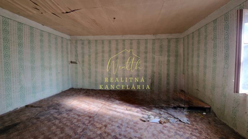 Pokoj v rodinném domě s poškozeným stropem, tapetami a podlahou s dřevěným dekorem.