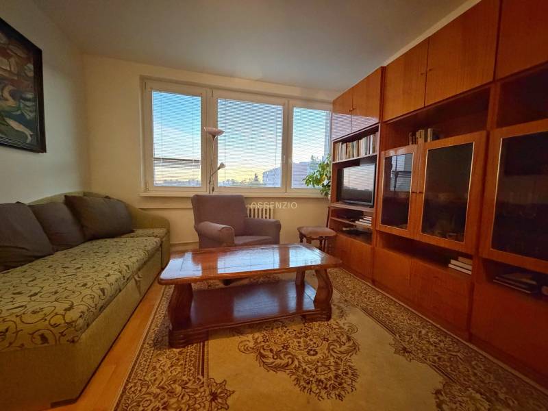 Obývací pokoj s pohovkou, křeslem, dřevěným nábytkem a podlahou s dřevěným dekorem ve 3pokojovém bytě.