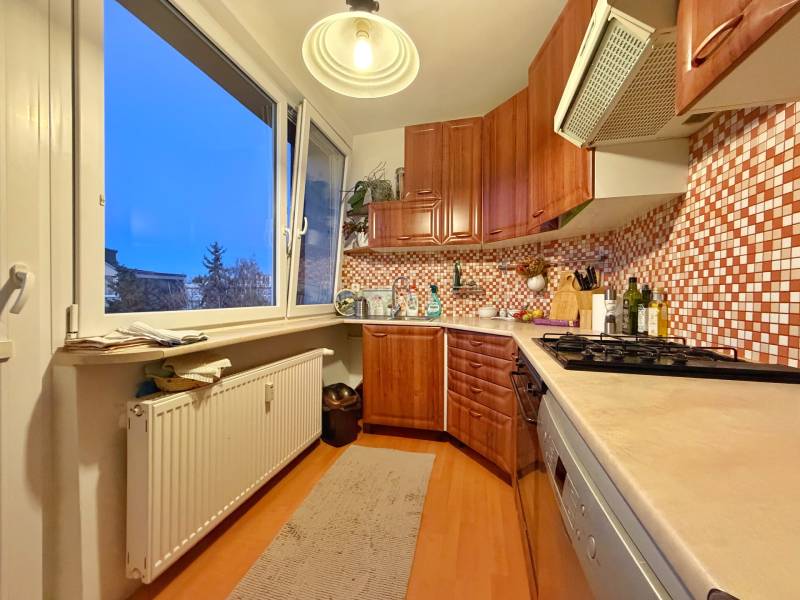 Kuchyně ve 3-pokojovém bytě se světlým nábytkem a podlahou s dřevěným dekorem.