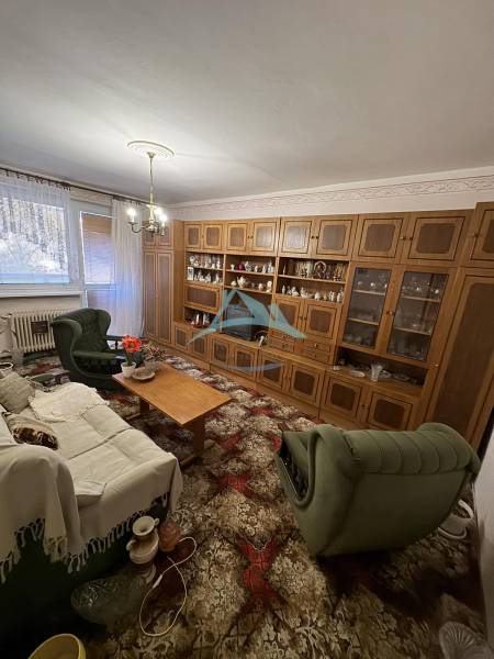 Obývací pokoj v 3-pokojovém bytě s dřevěnou obývací stěnou a zeleným nábytkem.