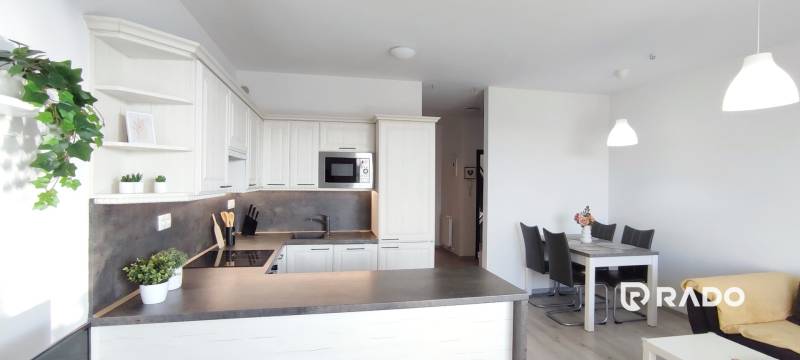 Kuchyně 2pokojového bytu s bílými skříňkami a jídelním stolem, podlaha s dřevěným dekorem.