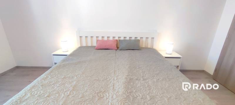 Ložnice s postelí, dvěma polštáři a nočními stolky v dvoupokojovém bytě.