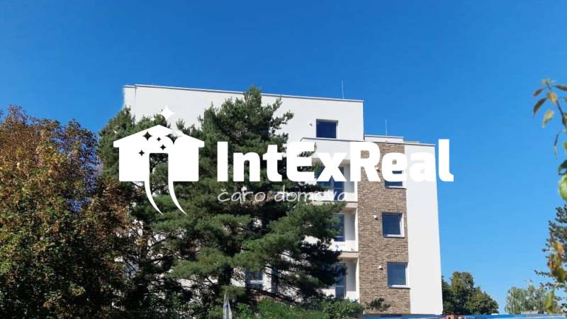 Budova na Športovní ulici v Galantě, obklopená stromy, s jasnou oblohou v pozadí.