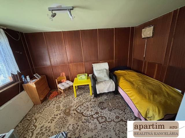 Pokoj se židlemi, lůžkem, skříňkou a dekorativním kobercem v Zahradách.