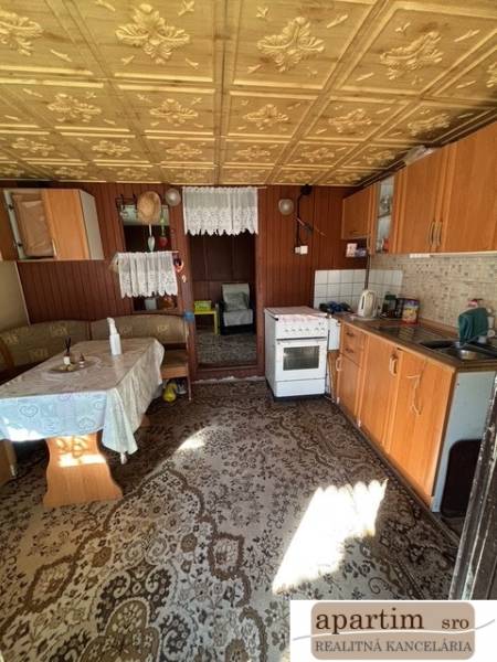 Kuchyně se starším nábytkem, podlaha s dřevěným dekorem, viditelná jídelní část.