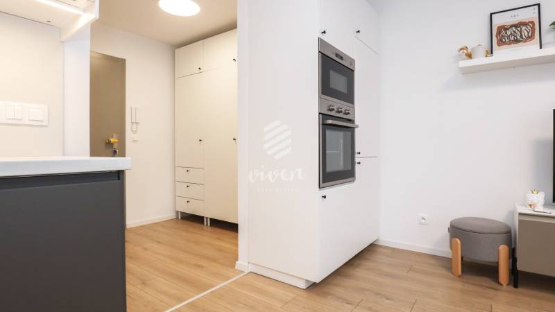 Kuchyně v 1-pokojovém bytě s bílými skříňkami a podlahou s dřevěným dekorem.