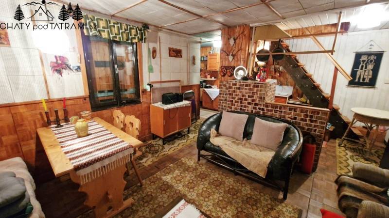 Interiér chaty s pohovkou, podlahou s dřevěným dekorem, jídelním stolem a schodištěm.