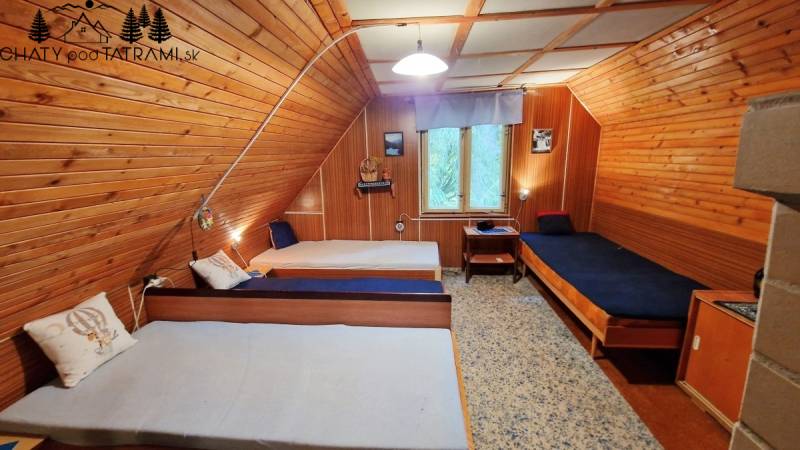 Dřevěný interiér chaty se třemi jednolůžkovými postelemi a krajinomalbou.