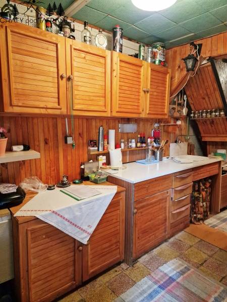 Kuchyně v chatě s dřevěnými skříňkami a bílou pracovní deskou, útulná atmosféra.