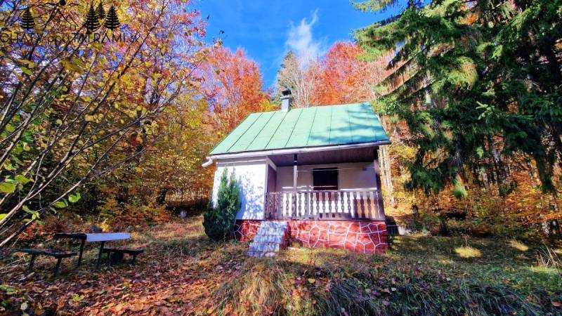 Chata na Tálach v Bystré obklopená barevnou podzimní přírodou s lavičkou v popředí.