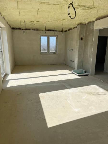 Prostorná místnost v rodinném domě na ulici Vyšná Šebastová se surovou omítkou a kabely.