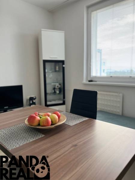 Jídelní stůl s mísou jablek, židle, skleněná vitrína, okno.