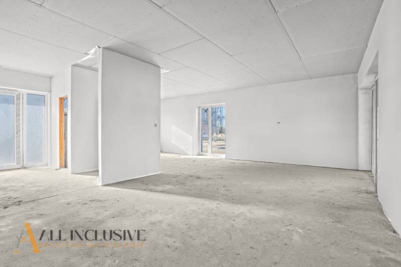 Prázdný interiér v rodinném domě s bílými stěnami a velkými okny.