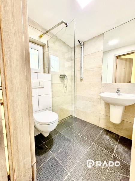 Koupelna v rodinném domě s proskleným sprchovým koutem a tmavou dlažbou.