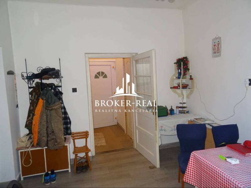 Interiér rodinného domu s podlahou s dřevěným dekorem, jídelním stolem a věšákem na oblečení.