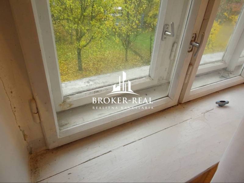 Pohled z okna v rodinném domě s výhledem na podzimní zahradu a stromem.