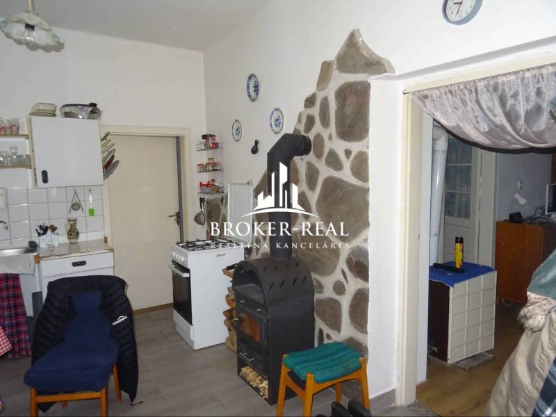 Kuchyně v rodinném domě se sporákem, pecí a kamenným obkladem u stěny.