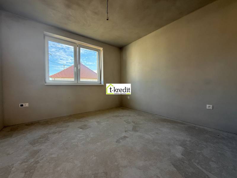 Pokoj v rodinném domě, stěny bez dekorací, vidět střechu sousední budovy.