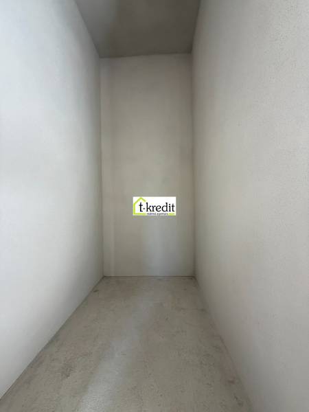 Úzký, prázdný interiér rodinného domu s betonovou podlahou a bílými stěnami.