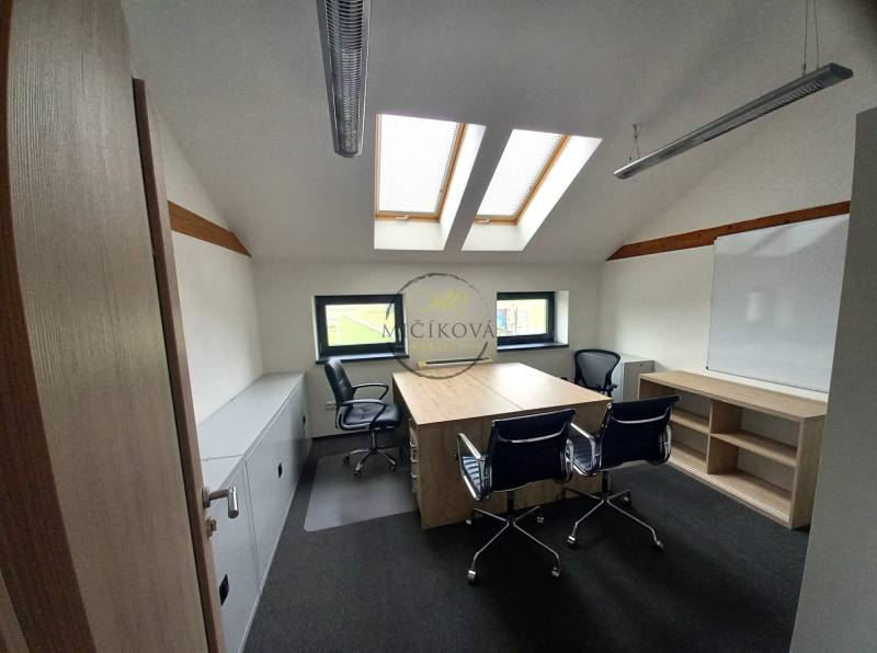Kancelář s podlahou s dřevěným dekorem, střešními okny a stoly se židlemi.