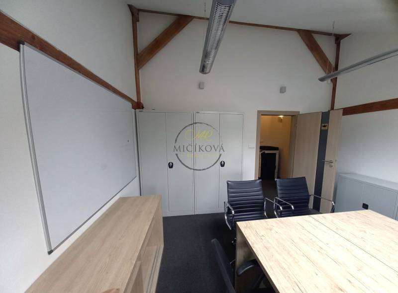 Kanceláře se stolem, černými židlemi, skříňkami a bílou tabulí.