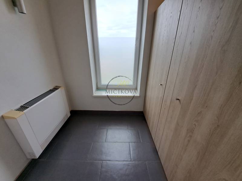 Kancelář s dlažbou, úložným prostorem a velkým oknem, bez nábytku.