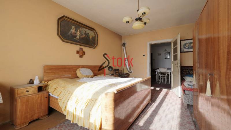 Ložnice v rodinném domě s dřevěným nábytkem, obrazem a lustrem.