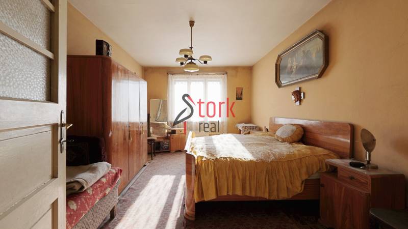 Ložnice v rodinném domě s nábytkem, lustrem a obrazem na stěně.