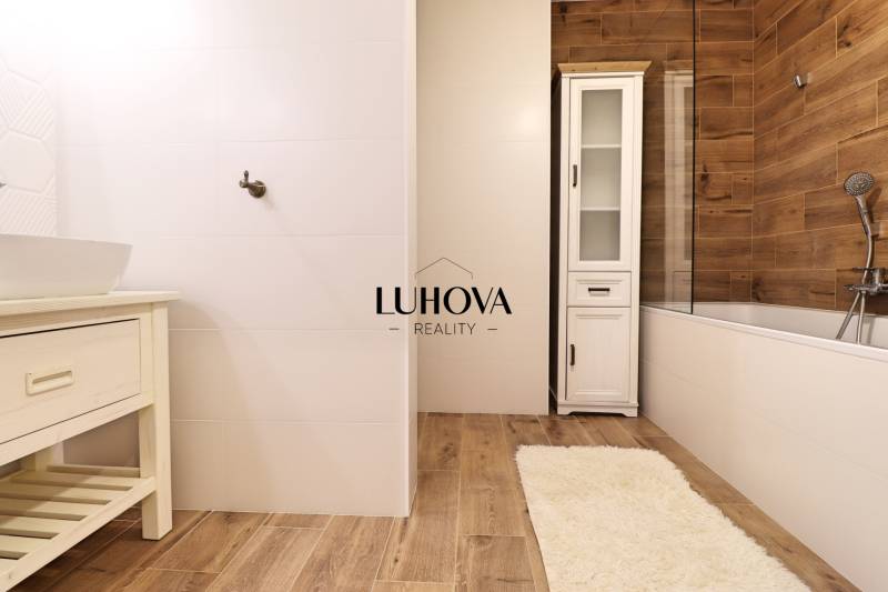 Koupelna s bílými obklady a podlahou s dřevěným dekorem v 3-pokojovém bytě.