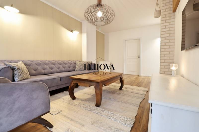 Obývací pokoj v 3-pokojovém bytě s pohovkou, dřevěným stolem a podlahou s dřevěným dekorem.