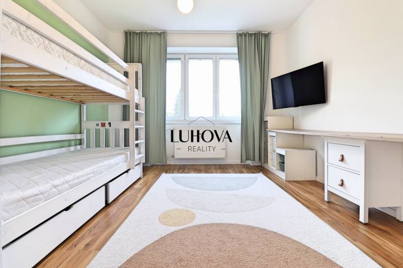 Pokoj ve 3-pokojovém bytě s patrovou postelí, televizí a podlahou s dřevěným dekorem.